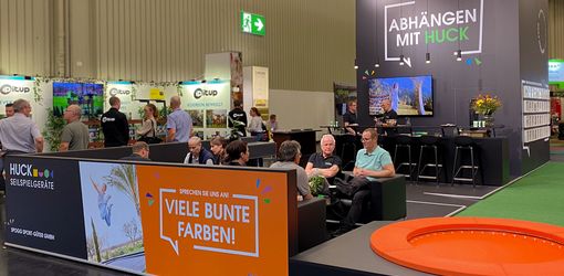 Trade fair booth, people sitting and talking, having coffee, orange trampoline.