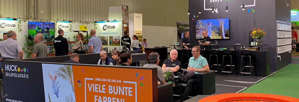 Trade fair booth, people sitting and talking, having coffee, orange trampoline.