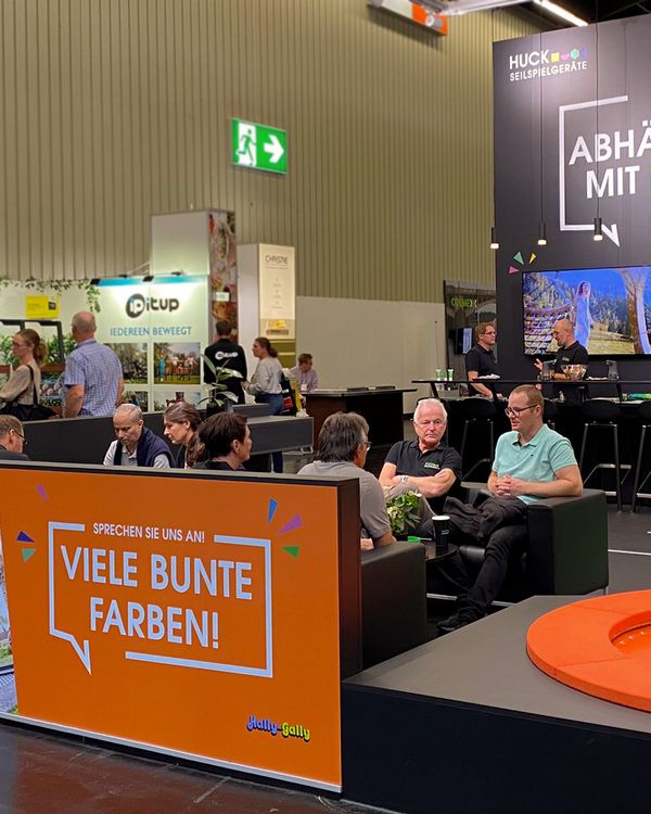 Trade fair booth, people sitting and talking, having coffee, orange trampoline.