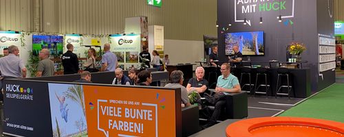 Trade fair booth, people sitting and talking, having coffee, orange trampoline.